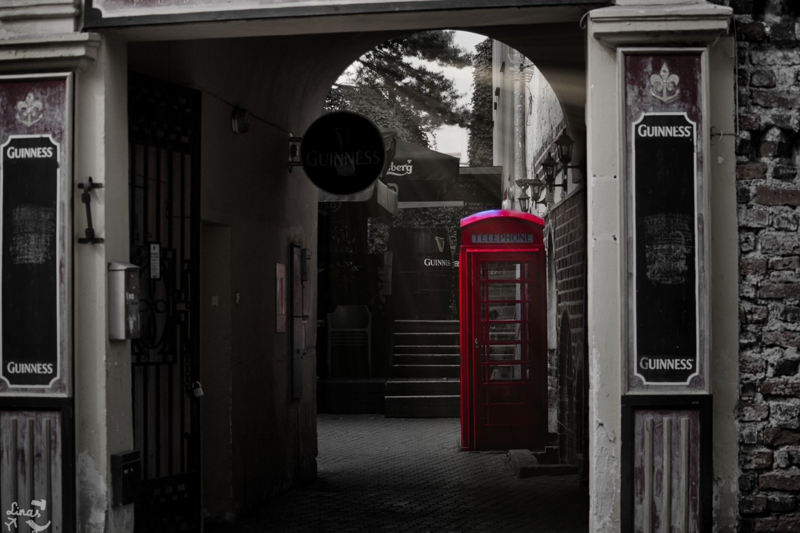 A black and white photo of a telephone booth in an inner courtyard, the telephone booth is the only coloured element in the photo.